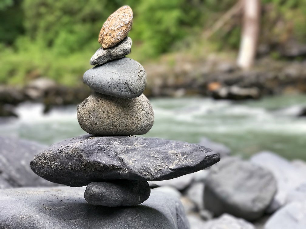 A small stone cairn of multi colored rocks next to a riverbank.