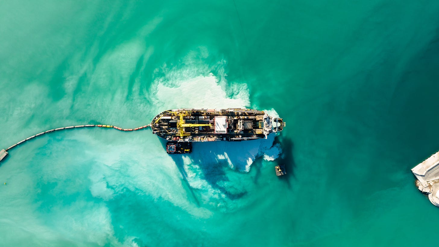 Aerial view of a cable-laying ship trailing its cable across open water to shore, the global network stitched line by line. Aerial view of a cable-laying ship trailing its cable across open water to shore, the global network stitched line by line.
