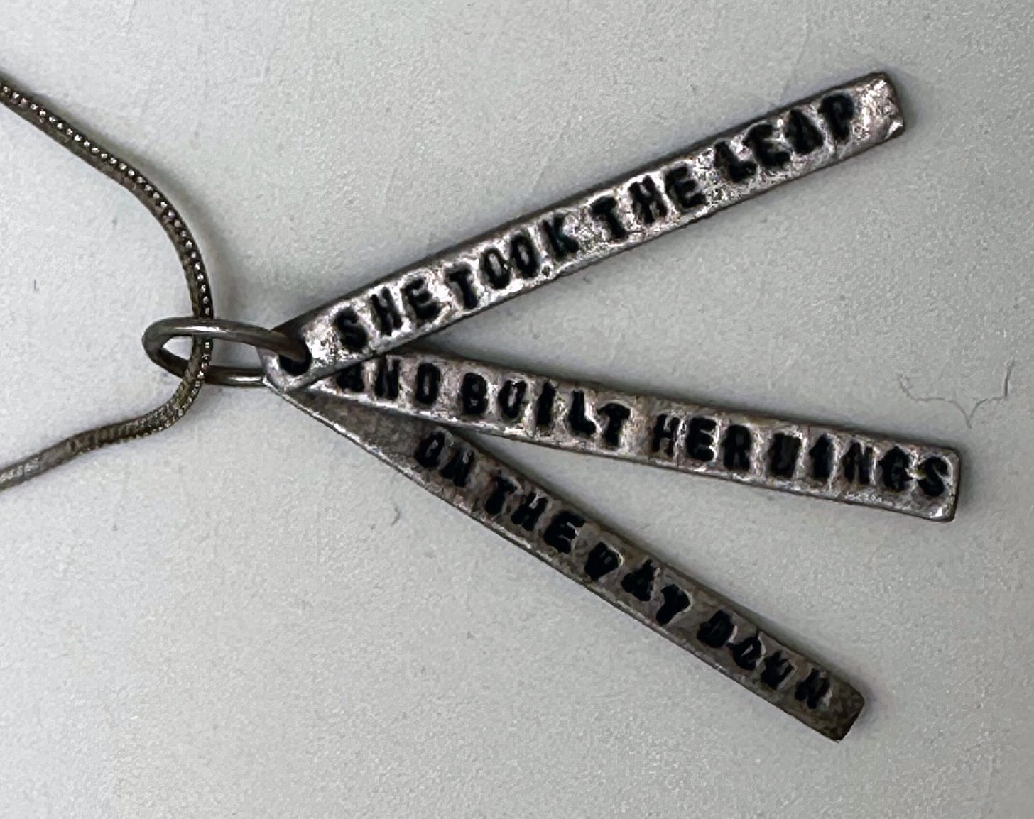 A silver necklace reading she took the leap and built her wings on the way down