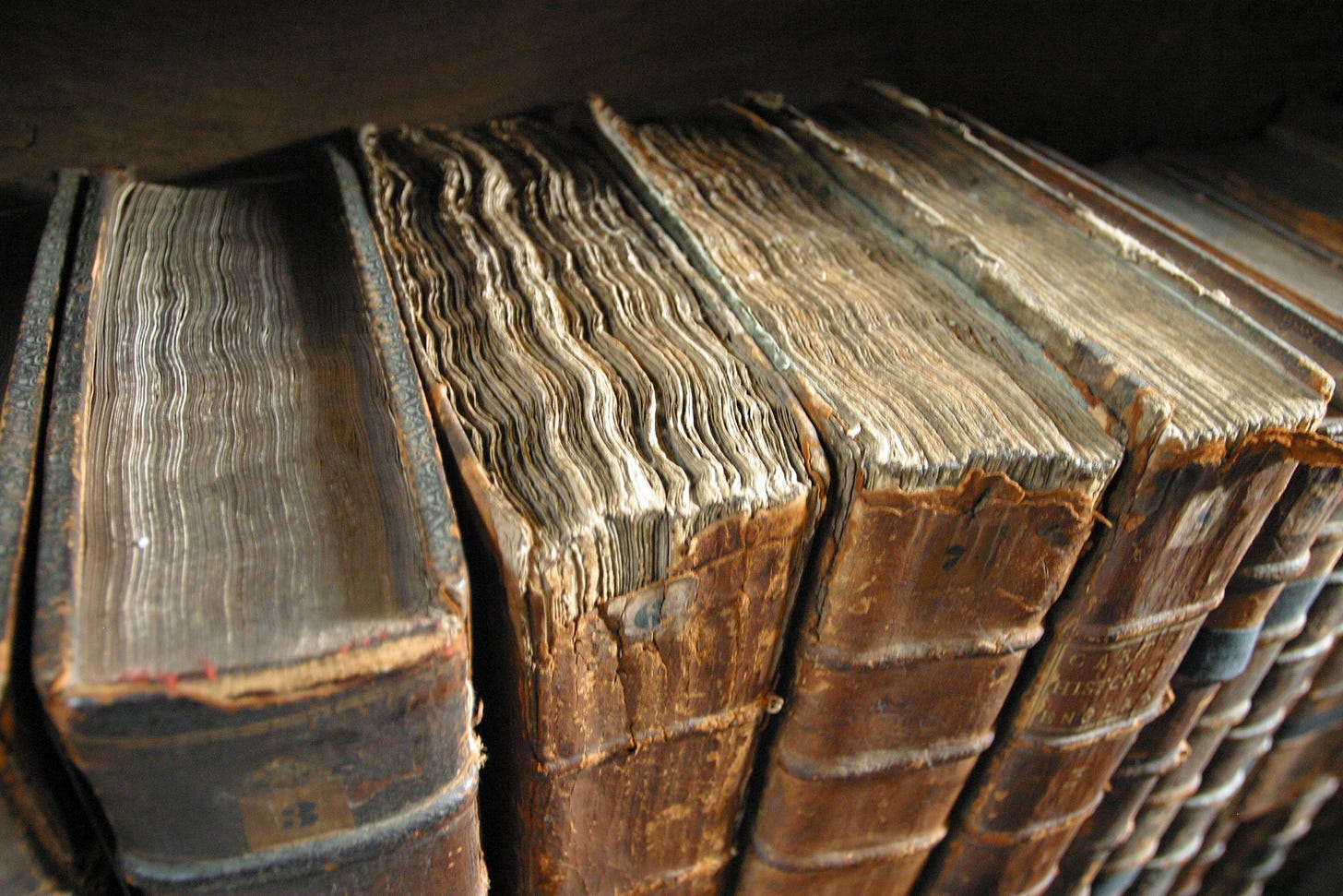 close up photo of several old books with broken spines on a shelf