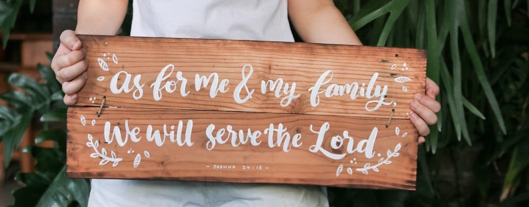 a woman holding a wooden sign that says as for me and my family we will