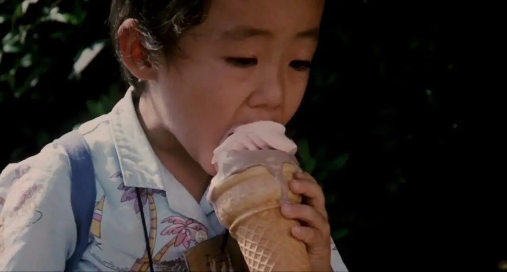 A child enjoys a melting ice cream cone outdoors. Wearing a floral shirt, the child appears focused and content.