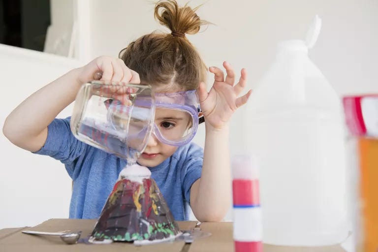young girl pouring liquid into volcano model