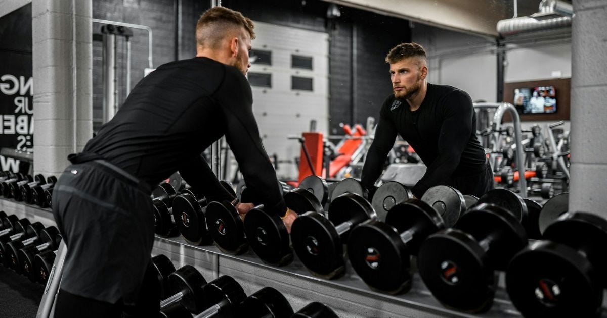 Man in black long sleeve shirt and black pants carrying black dumbbell Man in black long sleeve shirt and black pants carrying black dumbbell