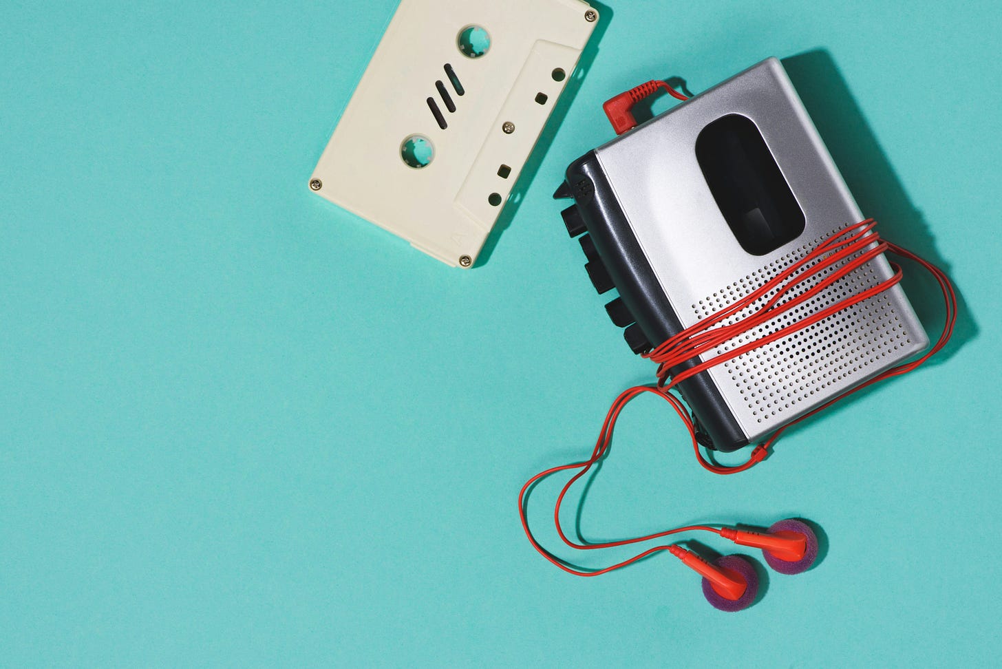 A vintage walkman, red earbuds, and a white cassette tape on a blue background