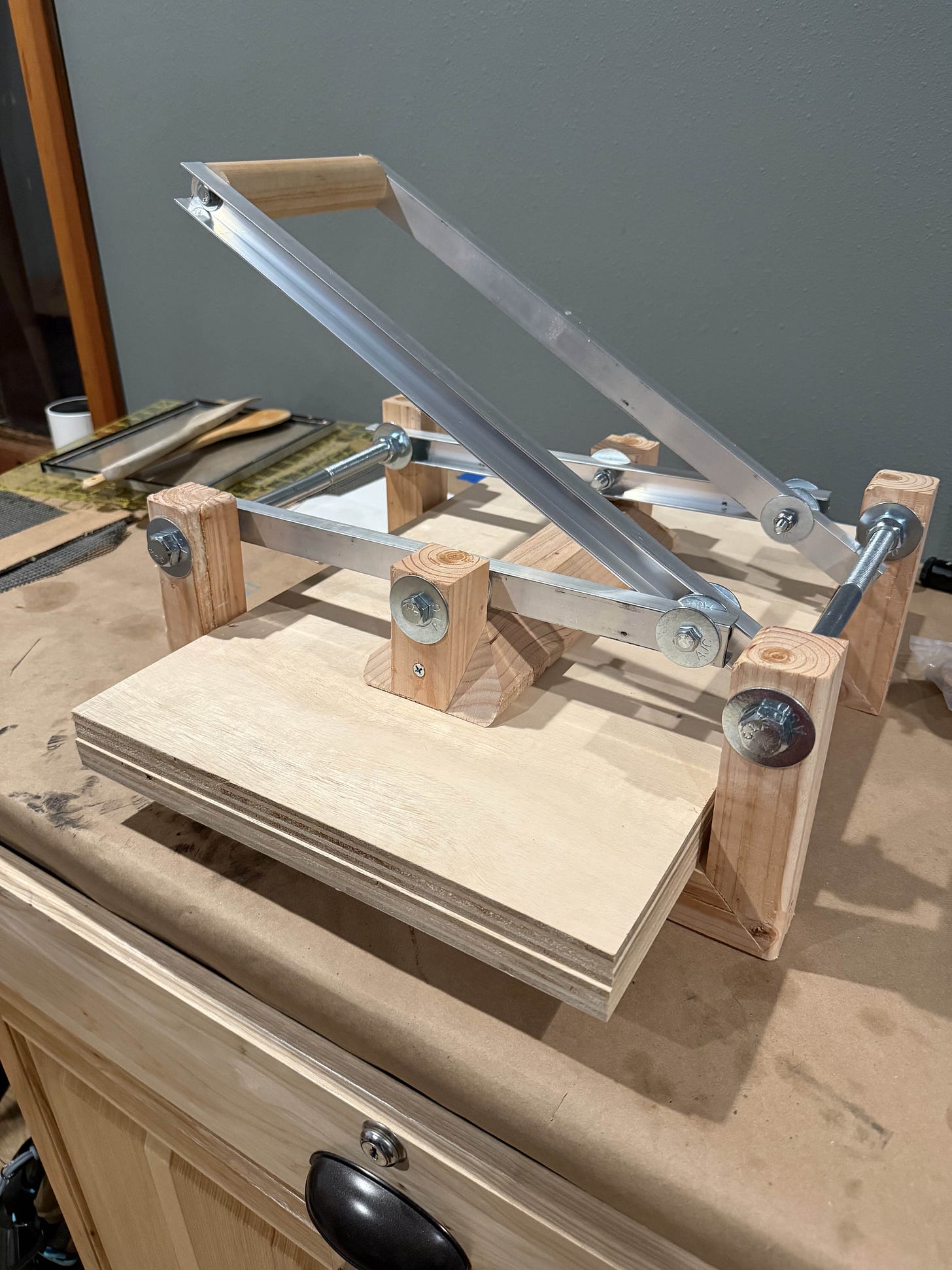 A homemade printmaking press built from hardware-store materials, sitting on a paper-covered work surface.
