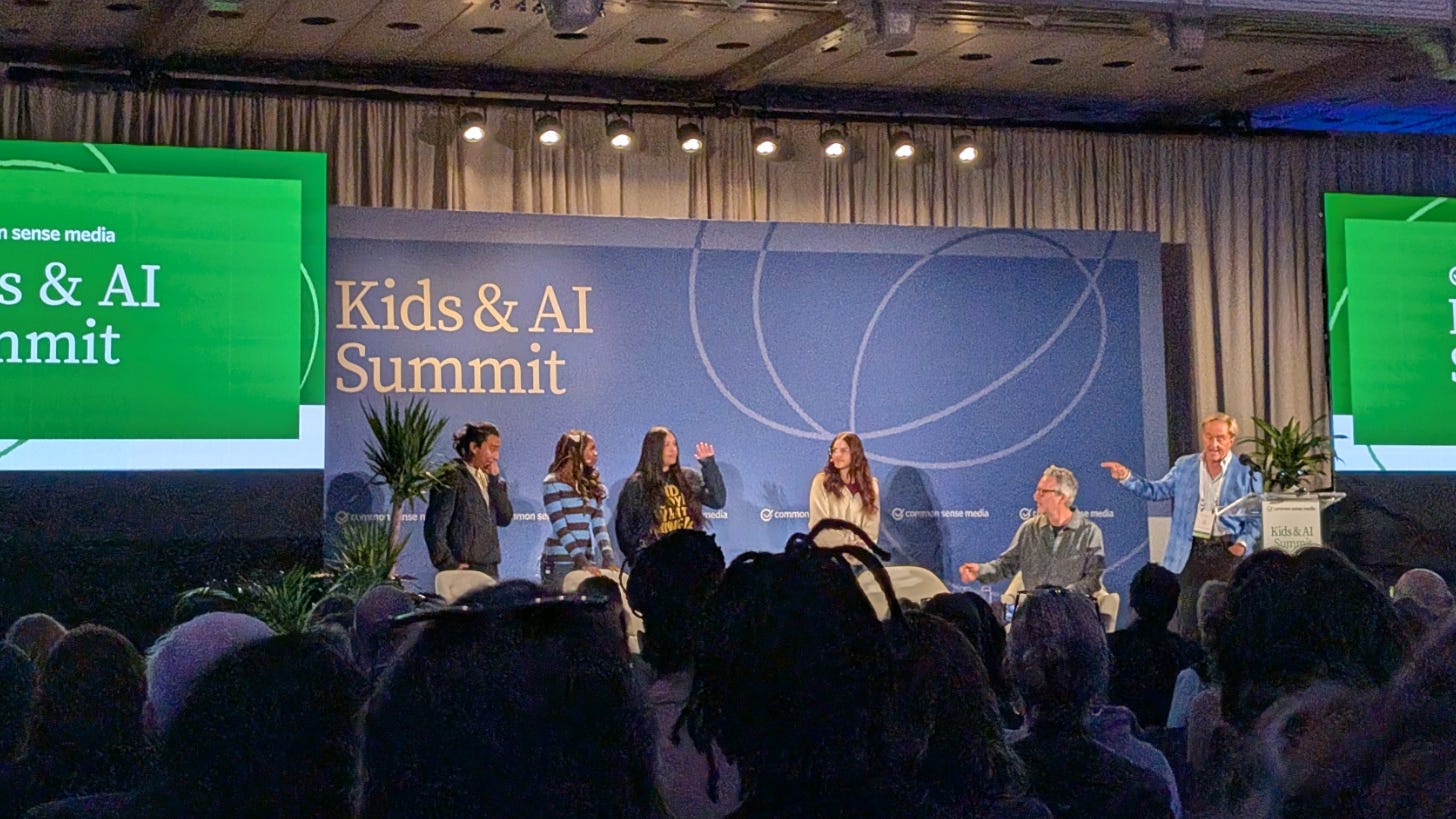 Four high school students stand on stage at the Kids & AI Summit while Jim Steyer points toward them Four high school students stand on stage at the Kids & AI Summit while Jim Steyer points toward them