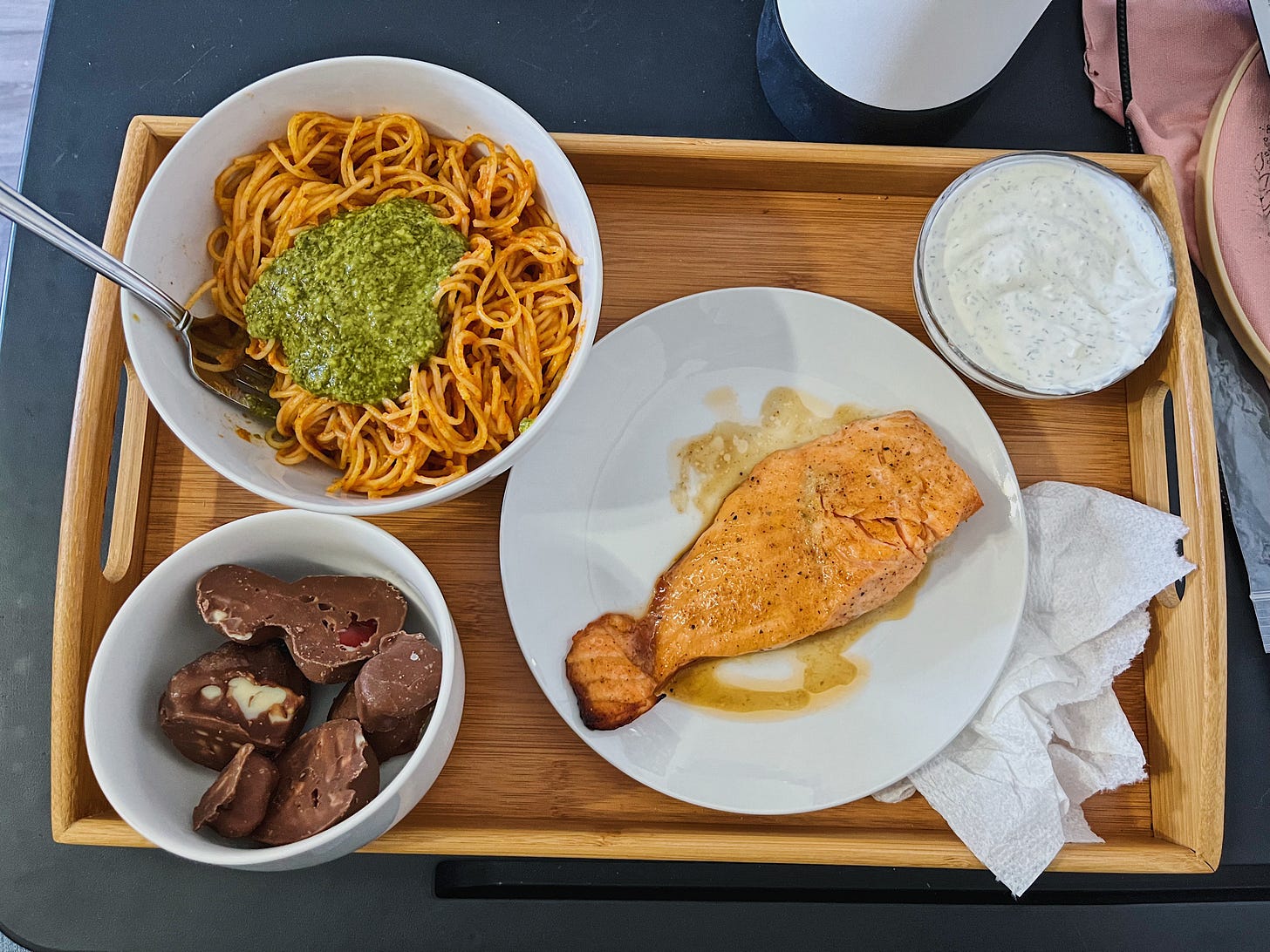 A tray with a white bowl of creamy orange spaghetti, a small bowl of chocolate, and a plate of salmon with a ramekin of dipping sauce. A tray with a white bowl of creamy orange spaghetti, a small bowl of chocolate, and a plate of salmon with a ramekin of dipping sauce.