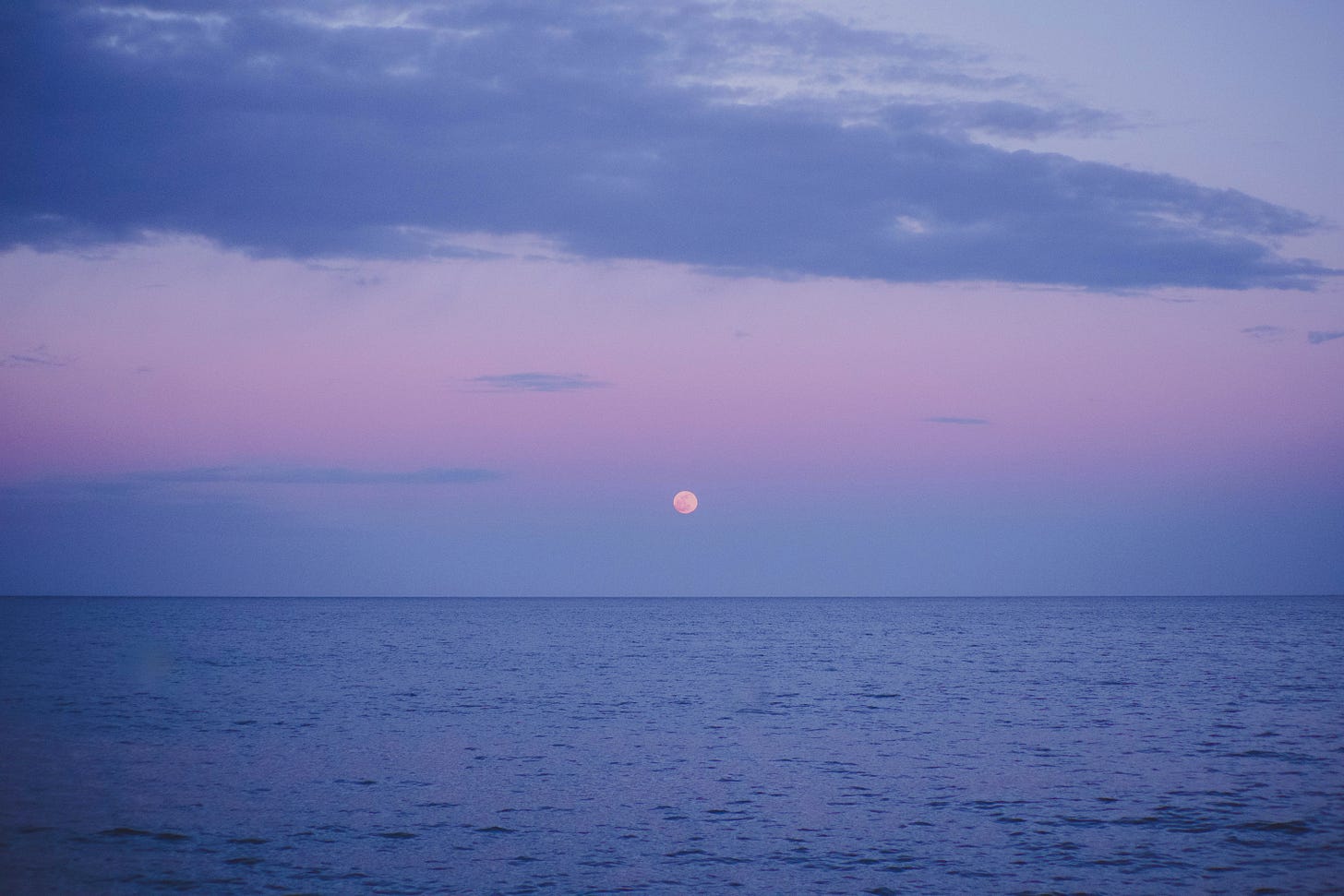 moon rise over the ocean with purple clouds