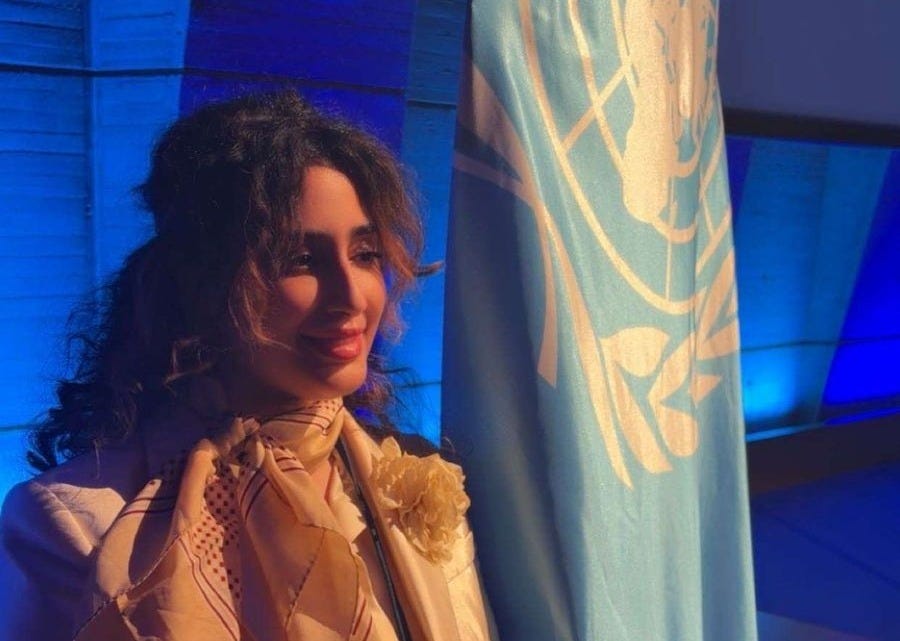 Abeer Al-Saud, a creative and humanitarian explorer, stands poised in front of a blue background and the United Nations flag