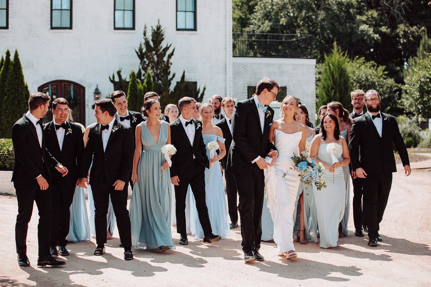 a wedding party in blacks and blues in front of a white brick building a wedding party in blacks and blues in front of a white brick building
