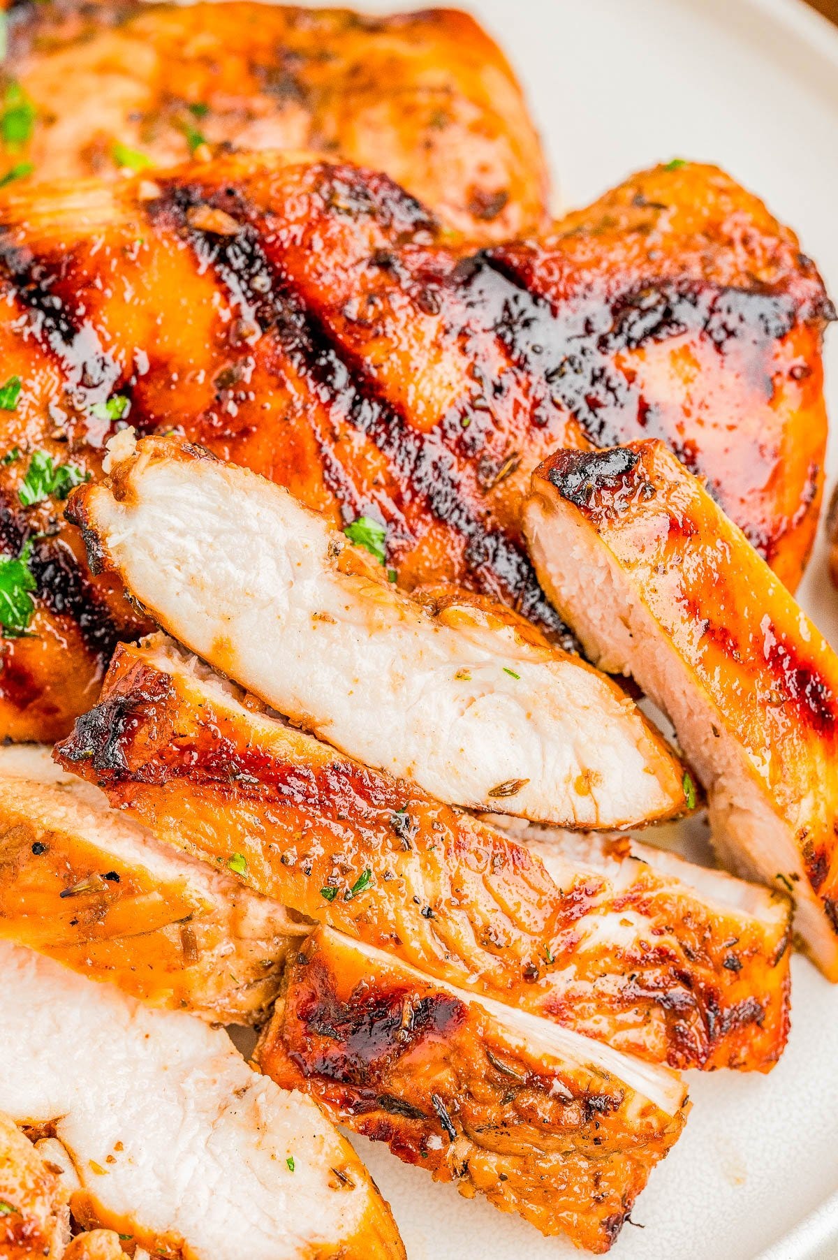 Close-up of grilled, sliced chicken breast with a golden-brown, slightly charred exterior, served on a white plate.