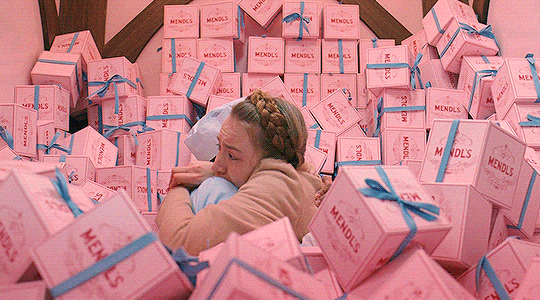 This may contain: a woman is surrounded by pink boxes with blue ribbons on them and wrapped in bows