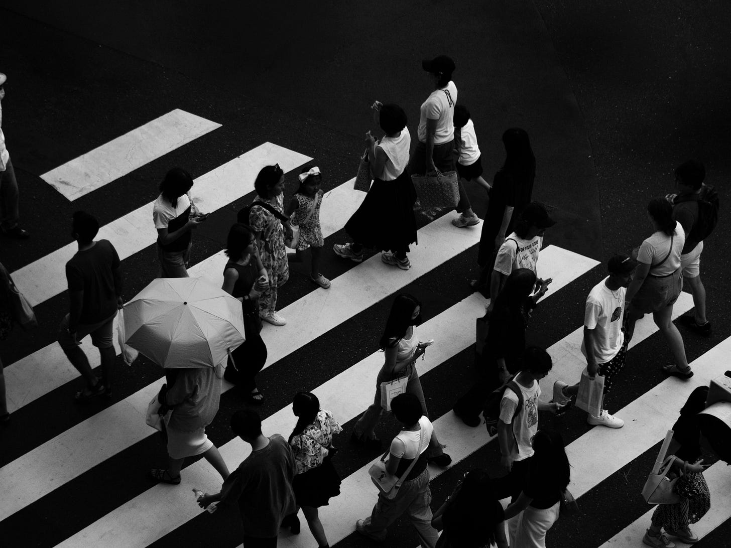 Aerial view of people crossing a zebra crossing on a city street, captured in striking monochrome.