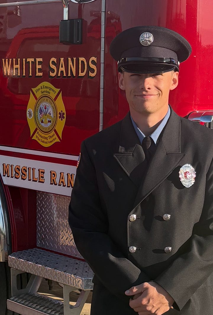 young man in fire uniform poses in front of a red engine. young firefighter in a burning forest in a national forest helmet 