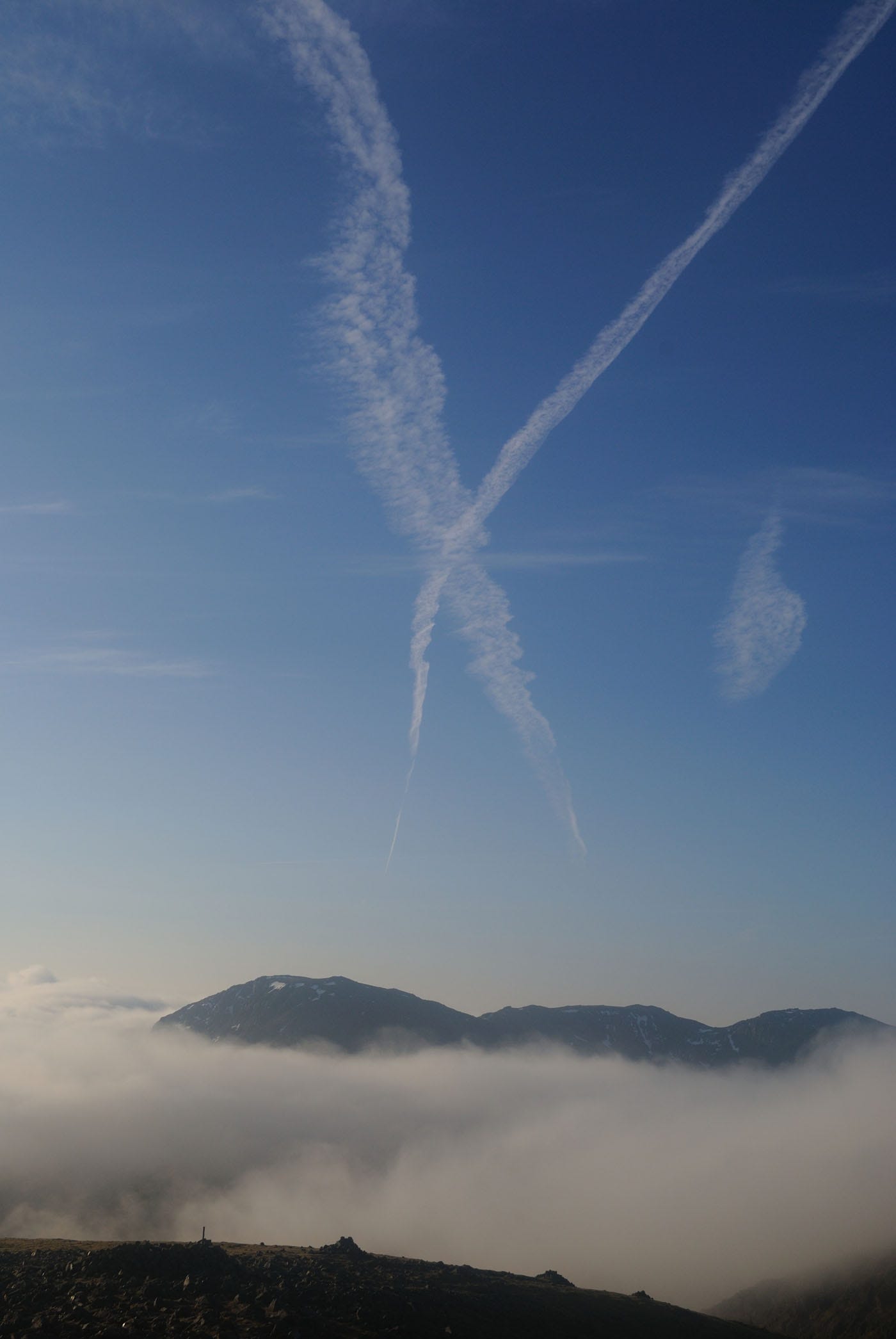 white vapour trails on blue sky, cloud and hills below