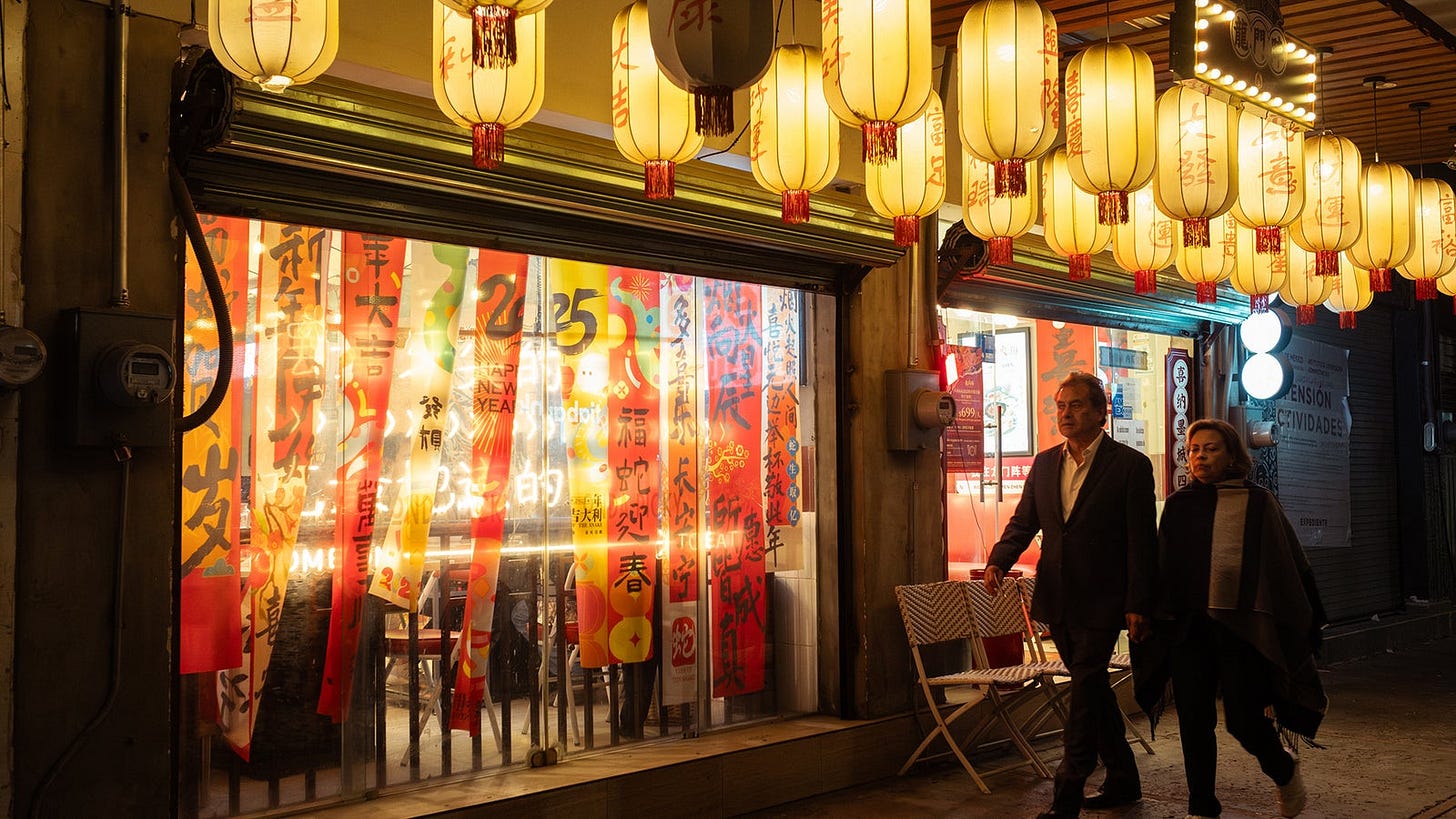 A couple walks past a restaurant adorned with red and yellow lanterns and colorful New Year decorations.