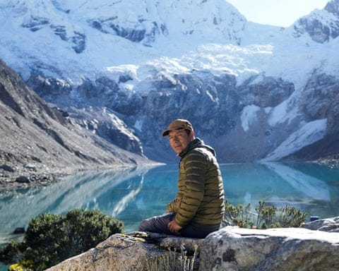 Man sitting on rock in front of a glacial lake, with glaciers in background Man sitting on rock in front of a glacial lake, with glaciers in background
