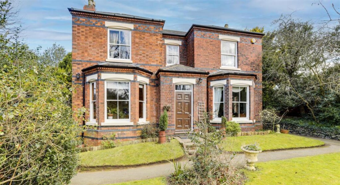 A large brick house with windows in front of a lawn with a path running through it, and hedges around it