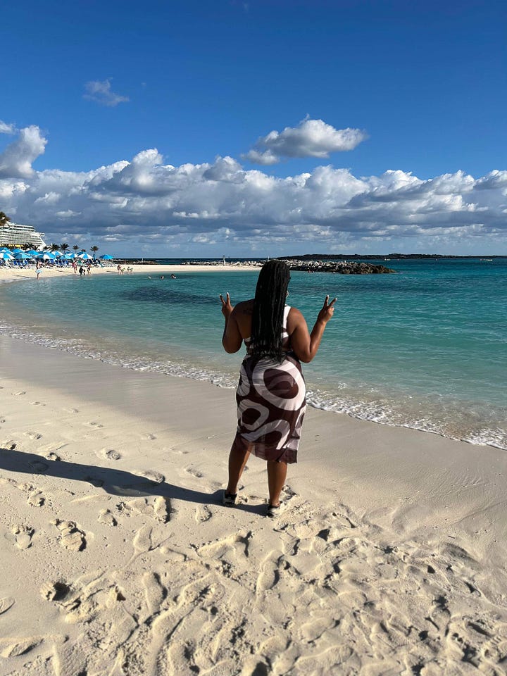 Black woman poses on a cruise ship in a multicolored purple dress. Black woman faces toward the Bahamian Ocean holding out the peace sign on each side.