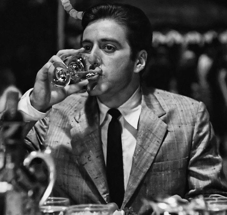 This may contain: a man sitting at a table drinking from a wine glass in front of his face