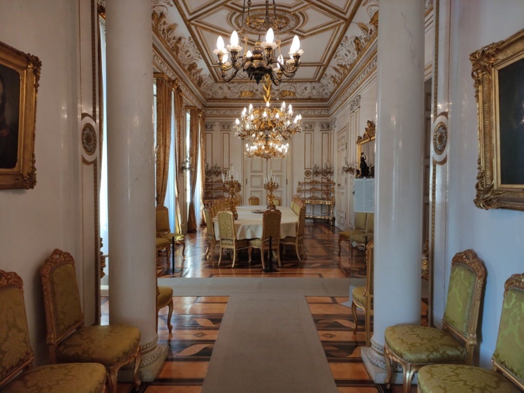 Walls are white and decorations, including the chairs, gold in the dining room, seen through the two pillars that mark the entrance from the next room
