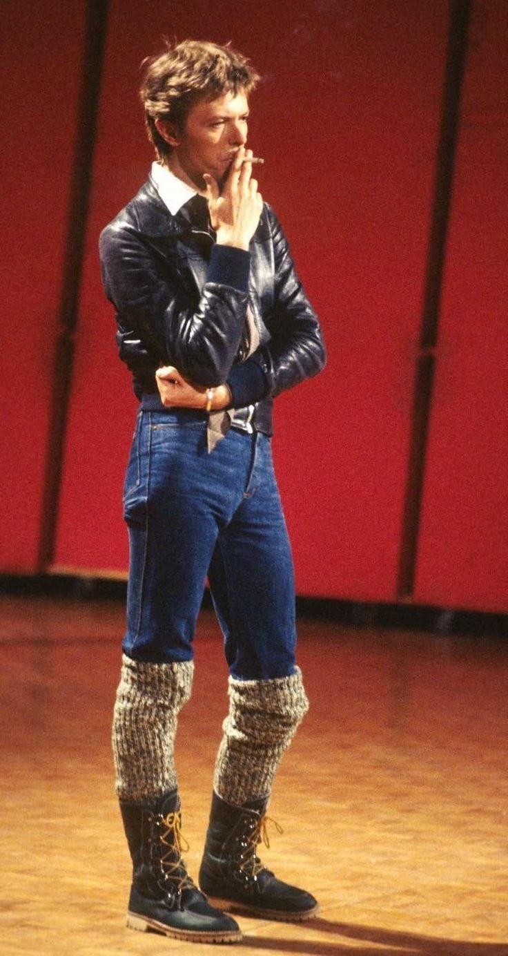 This may contain: a man standing on top of a wooden floor next to a red wall and wearing boots