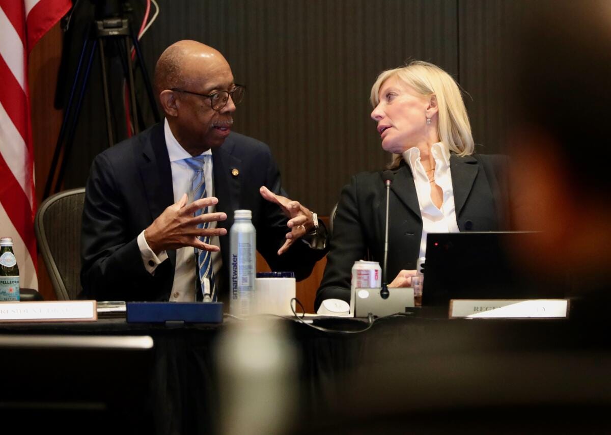 A man and a woman talk while sitting at a board room table at UCLA. 
