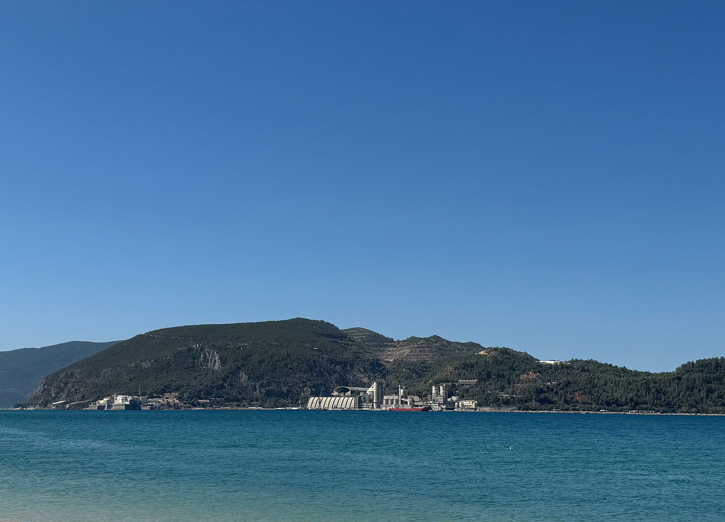 A beach view with a factory at the foot of green hills. A beach view with a factory at the foot of green hills.