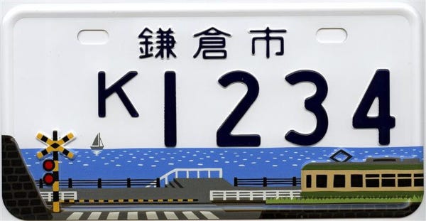 La plaque d'immatriculation représentant le passage à niveau d'Enoden, stylisé, vert et jauen devant la mer bleue