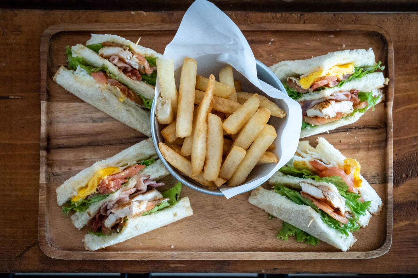 Triangle sandwiches with a bowl of chips in the middle all on a board Triangle sandwiches with a bowl of chips in the middle all on a board