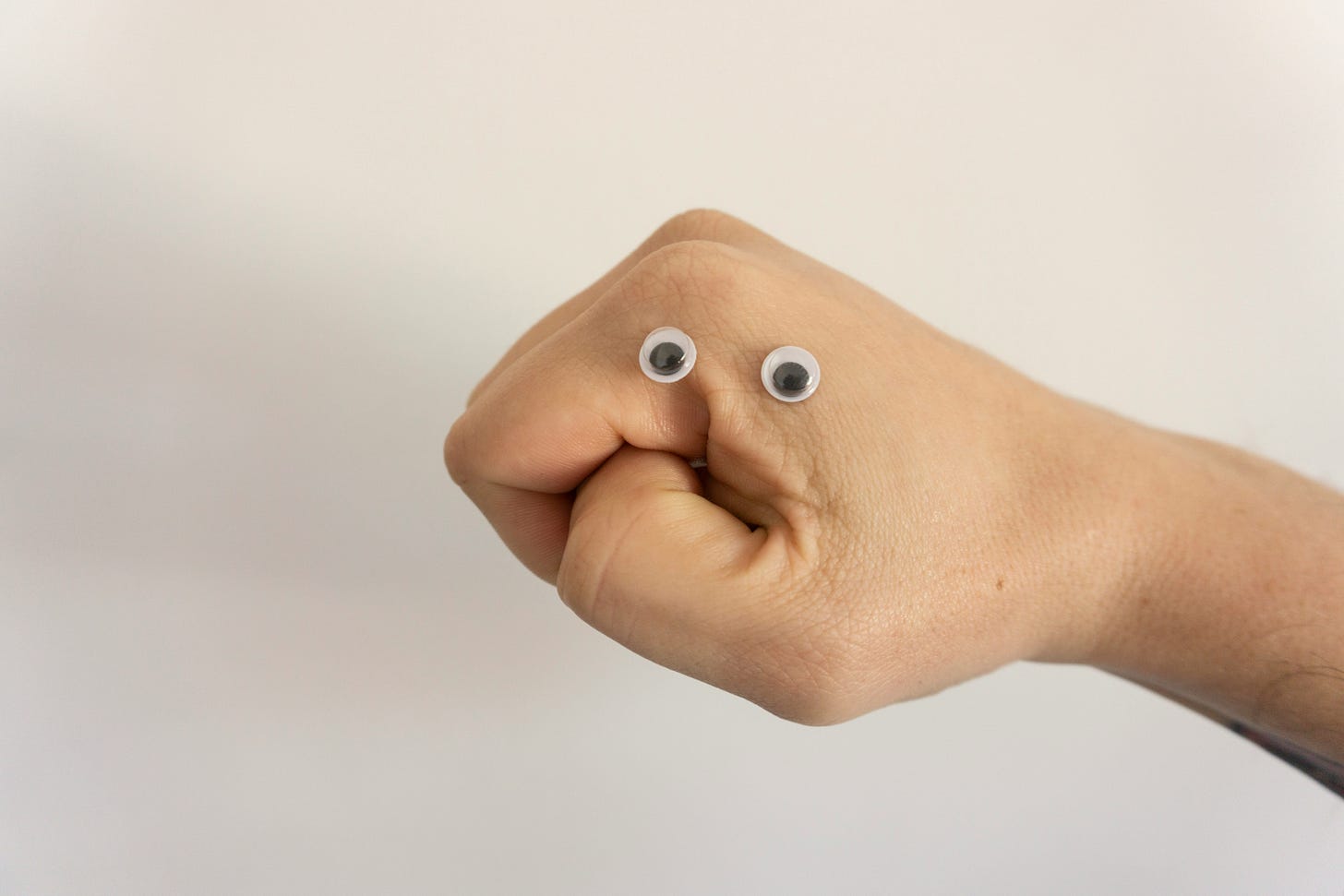 Hand in fist with thumb facing forward. Googly eyes stickers turn fist into face with an expression of uncertainty or dislike.