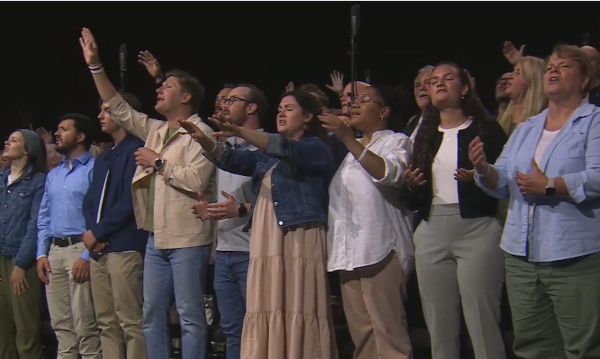 Group of people singing, some with hands partially outstretched Group of people singing, some with hands partially outstretched