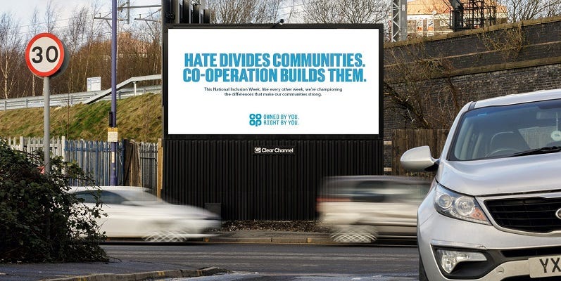 A photograph of a billboard by Co-op. The billboard reads 'Hate divides communities, co-operation builds them'.