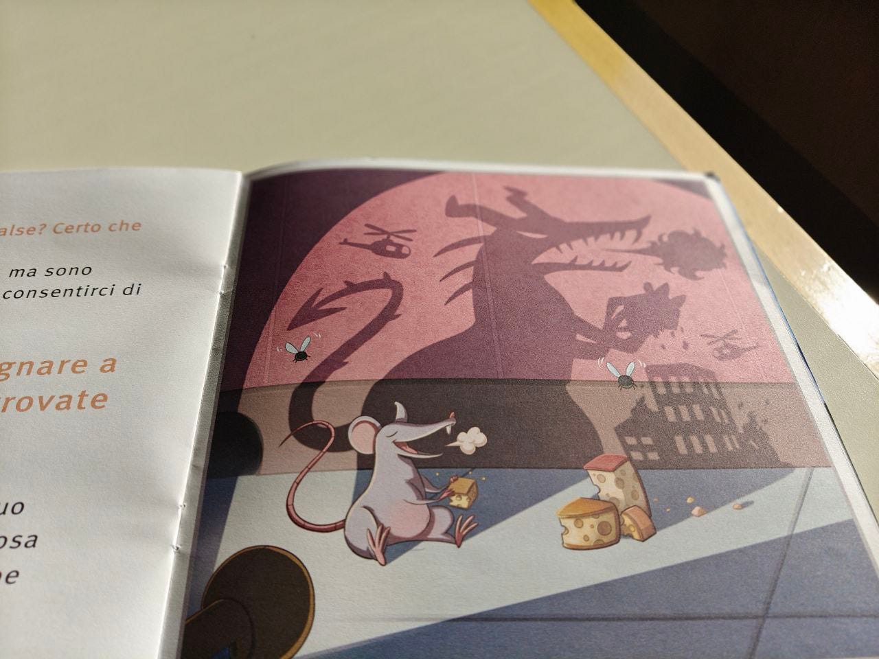 Pagina disegnata della Scatolina effequ FALSO. Seduto per terra c'è un topolino grigio a occhi chiusi che sta per gustarsi un pezzo di formaggio, mentre accanto ci sono altri tre pezzettini; due mosche si agitano sopra di lui perché sul muro retrostante la sua ombra disegna il contorno di un gigantesco drago intento a distruggere i palazzi di una città. La pagina è appoggiata su un tavolo color bianco sporco, e nell'angolino in alto a destra si intravede nel buio un pezzo di muro.