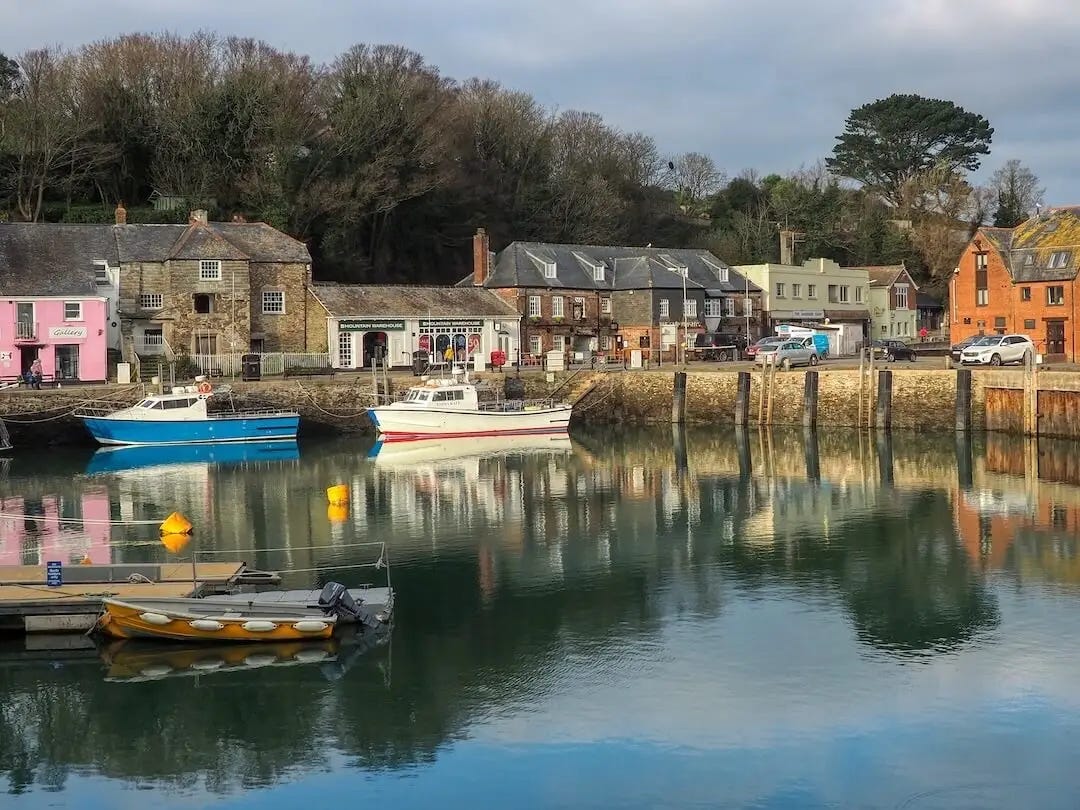 Reflections of boats in a harbour surrounded by cottages