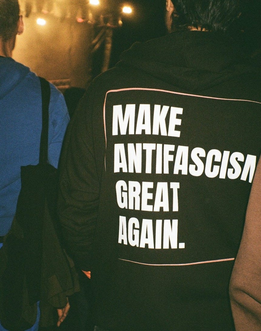 Person wearing hoodie with 'make antifascism great again' text.