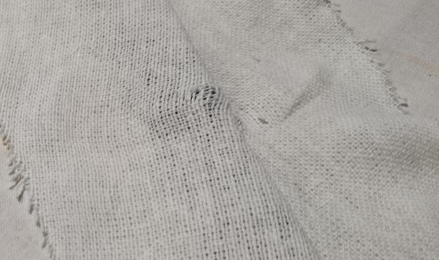 two pieces of cloth sewn together, and tugged on harshly. the weave in the centre has spread and torn