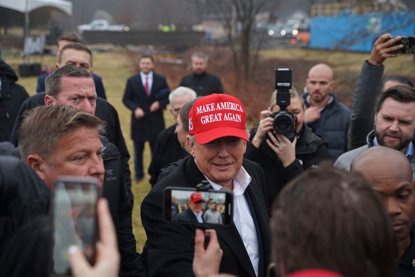 Donald Trump in a red MAGA cap surrounded by a crowd and cameras in East Palestine.