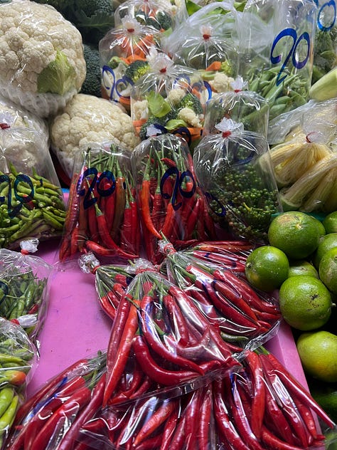 Outdoor farmers market in Chiang Mai with multicolored eggs, rows of produce, meats, and crickets.