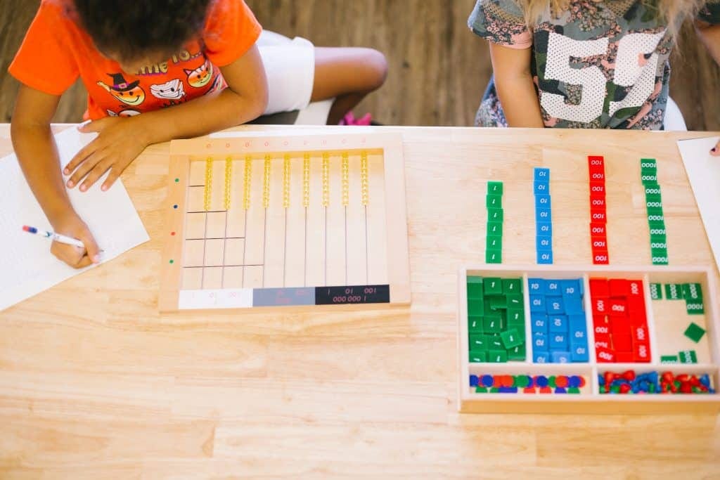 Two children using Montessori math materials including bead chains and stamp game — what is Montessori mathematics work