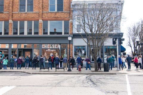 Street view showing two lines of people standing on a pavement with shopfronts behind them. Street view showing two lines of people standing on a pavement with shopfronts behind them.