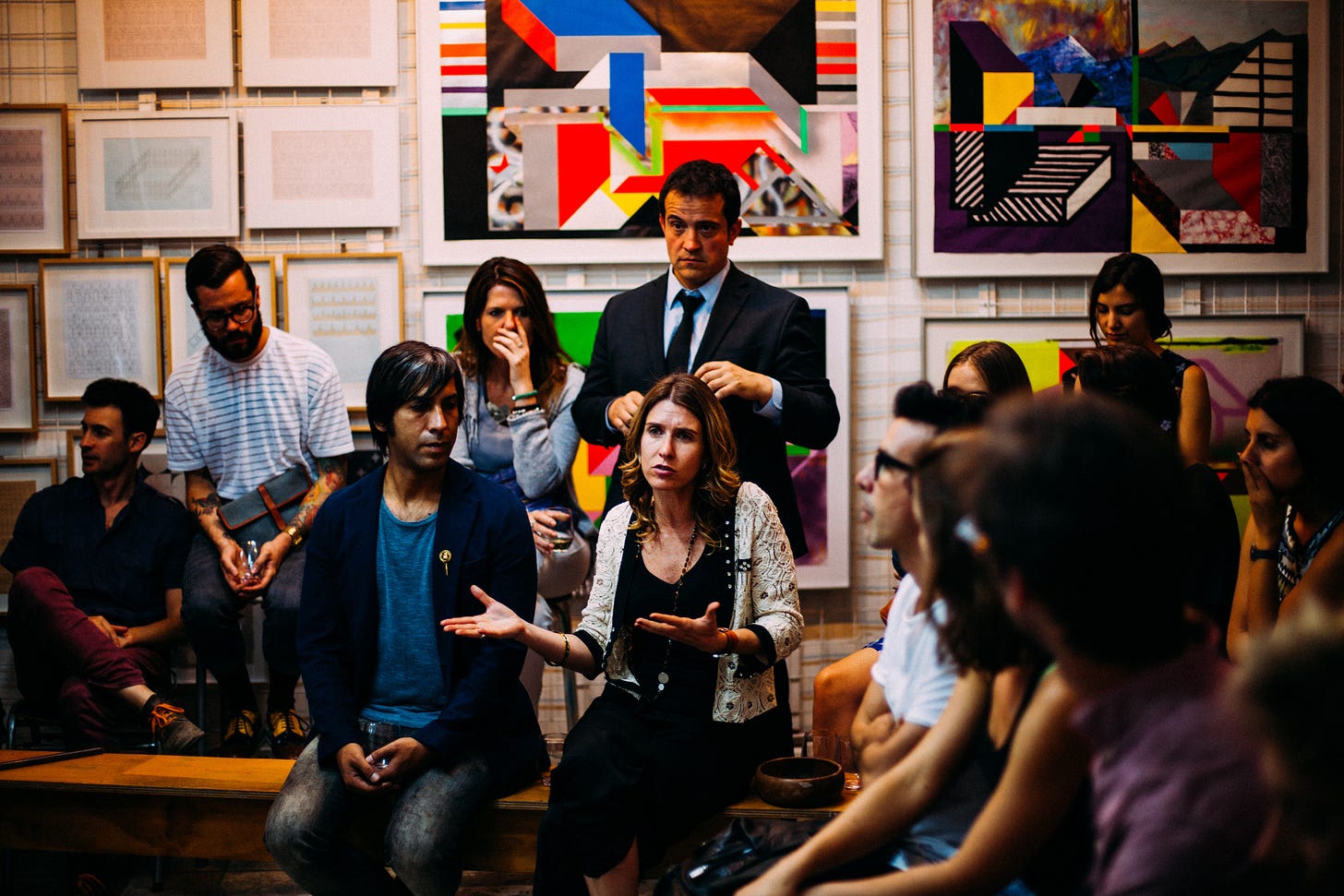 A group of people are conversing in a room. The focus is on a woman who is gesticulating with her hands.