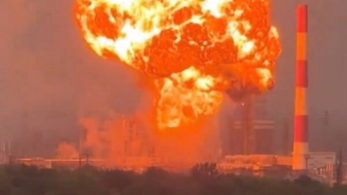 A huge fireball and thick smoke rise above the Novokuibyshevsk oil refinery in Russia after a drone strike, with a red-and-white smokestack visible nearby.