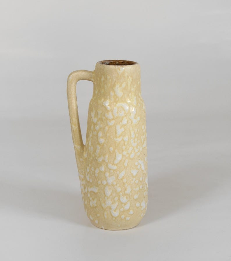 May include: A yellow ceramic vase with a white speckled glaze and a handle. The vase is about 15 cm tall.