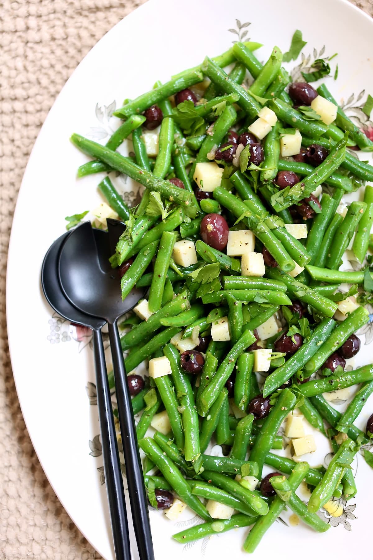 a white platter with green bean salad on it and black utinsils