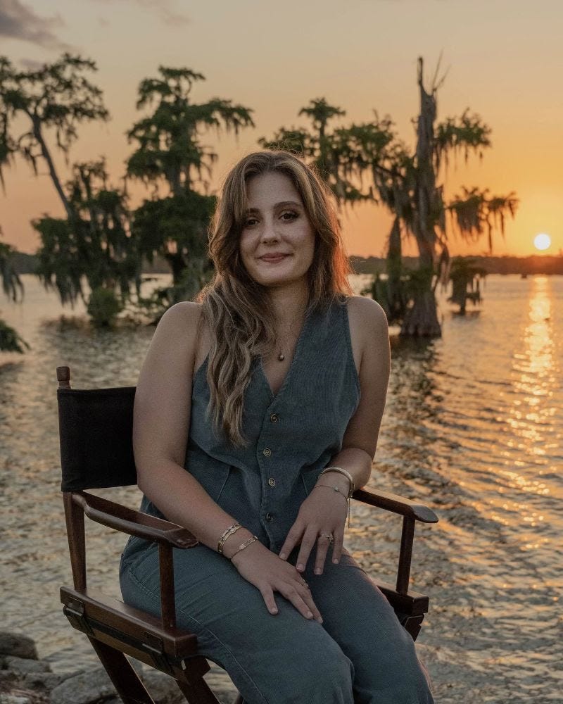 A photograph of author Jordan LaHaye Fontenot, seated and smiling in front of a bayou sunset