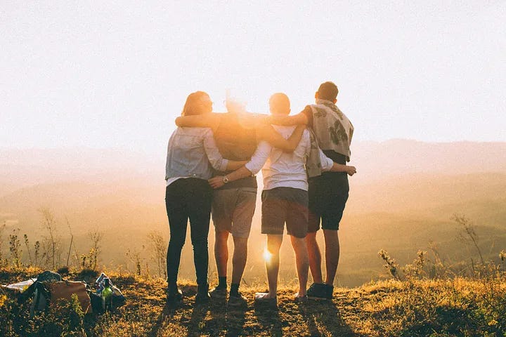 four young adults arm-in-arm, facing toward hazy mountains and the streaming sun four young adults arm-in-arm, facing toward hazy mountains and the streaming sun