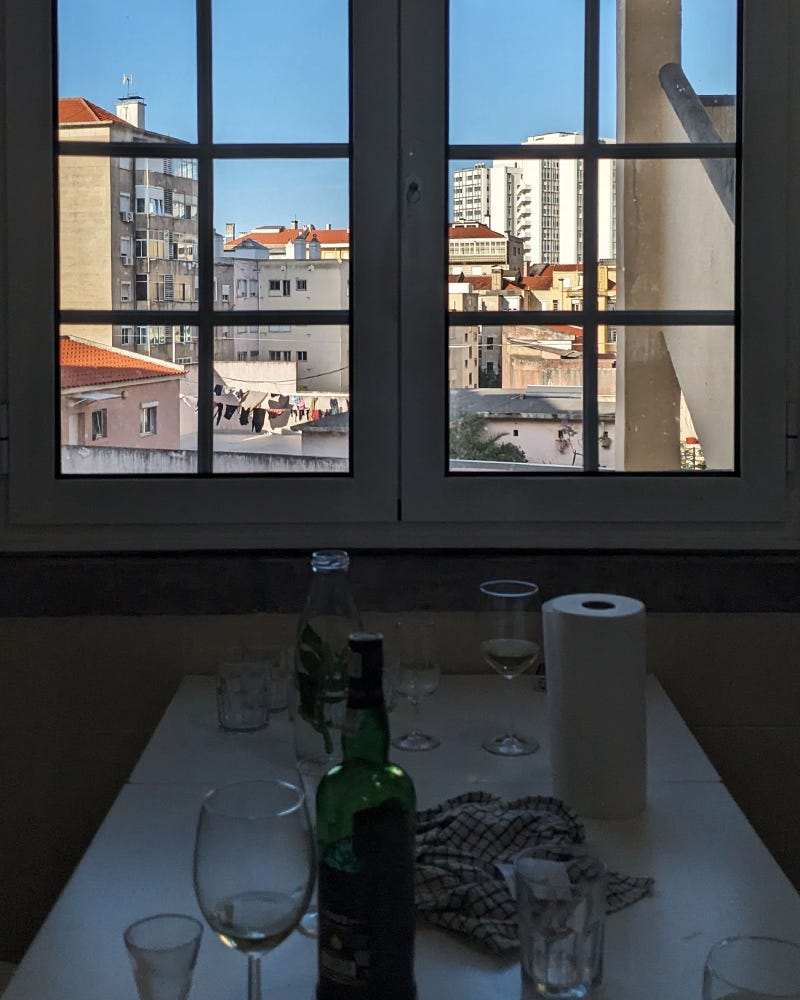 Photo of a window looking out to buildings and a laundry line in Lisbon. There are glasses and a bottle of port on the table in the foreground. Photo of a window looking out to buildings and a laundry line in Lisbon. There are glasses and a bottle of port on the table in the foreground.