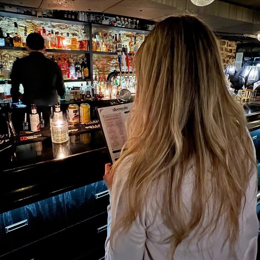 Blonde woman on a date sitting at a bar, reading a menu by candlelight